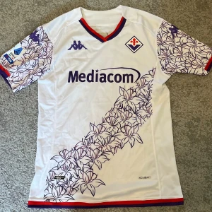 Fiorentina 23/24 - Fiorentina bortaställ under 23/24 säsongen. Tröjan är i storlek S men passar S-M. Den är i nyskick och är därmed som ny. Pris kan diskuteras. Skriv gärna om ni har några frågor eller funderingar!