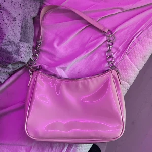 Beige axelväska med kedjedetaljer - Säljer en superfin beige axelväska i syntetmaterial med glansig finish. Väskan har en cool kedja som axelrem och en praktisk dragkedja upptill. Perfekt för både vardag och fest! 💖