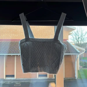 Grå stickad korsett från H&M - Säljer en superfin grå stickad korsett från H&M. Den har ett snyggt flätmönster framtill och breda axelband. Perfekt för lager-på-lager eller som den är. Passar både till vardags och fest!