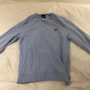 Ljusblå tröja från Lyle & Scott - Säljer en ljusblå tröja från Lyle & Scott i mycket bra skick. Den har en klassisk design med ett broderat emblem på bröstet. Tröjan är långärmad och passar perfekt för alla årstider.