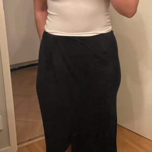 Svart långkjol - Säljer en stilren svart långkjol i bra skick. Kjolen har en enkel och elegant design. Den är gjord i ett mjukt och bekvämt material som faller fint längs kroppen.