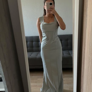 långklänning - Elegant ljusblå långklänning med en figurnära passform. Klänningen har en vacker, enkel design som passar perfekt för festliga tillfällen. Materialet ser ut att vara mjukt och följsamt, vilket ger en fin siluett.