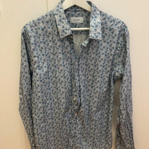 Blommig skjorta från Eton - Säljer en snygg blommig skjorta från Eton i super slim passform. Skjortan har ett detaljerat mönster i blått och vitt, perfekt för både vardag och fest. Den är långärmad och har klassiska knappar framtill. Passar bra till både jeans och kostymbyxor. Perfekt för vår och sommar! 🌸