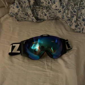 Bliz skidglasögon med blå spegelglas - Säljer ett par Bliz skidglasögon i fint skick (några repor på glaset men inget märkvärdigt)! De har blå spegelglas som ger ett coolt utseende och skyddar mot starkt solljus. Justerbart svart band med vit logga för perfekt passform. Perfekta för vinterns alla äventyr i backen! Kommer med en praktisk förvaringspåse.