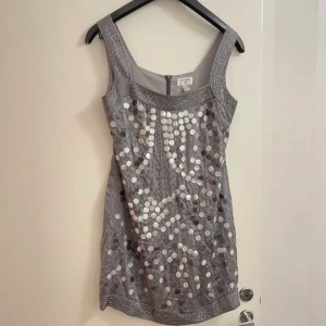 Grå paljettklänning - Snygg grå klänning med paljetter som ger en glittrig look. Perfekt för festliga tillfällen! Klänningen är ärmlös och har en kort längd, vilket gör den idealisk för en utekväll. Materialet känns lyxigt och bekvämt.