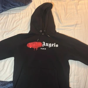 Svart hoodie från Palm Angels - Säljer en svart hoodie från Palm Angels med deras ikoniska logga i vitt och rött på framsidan. Skick 10/10 använd några få gånger! Kommer i storlek L men passar även M! Skriv för mer bilder eller frågor!