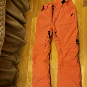 Rosa överdragsbyxor från Dope  - Säljer ett par snygga rosa överdragsbyxor från Dope i  bra skick. De har en mid/låg midja och dragkedjor vid fickorna för extra säkerhet och har även ventilation. Perfekta för vintern och vinteraktiviteter. Byxorna är gjorda i ett slitstarkt material och har en modern, loose passform. (OBS färgen ser lite orange ut på bilderna)