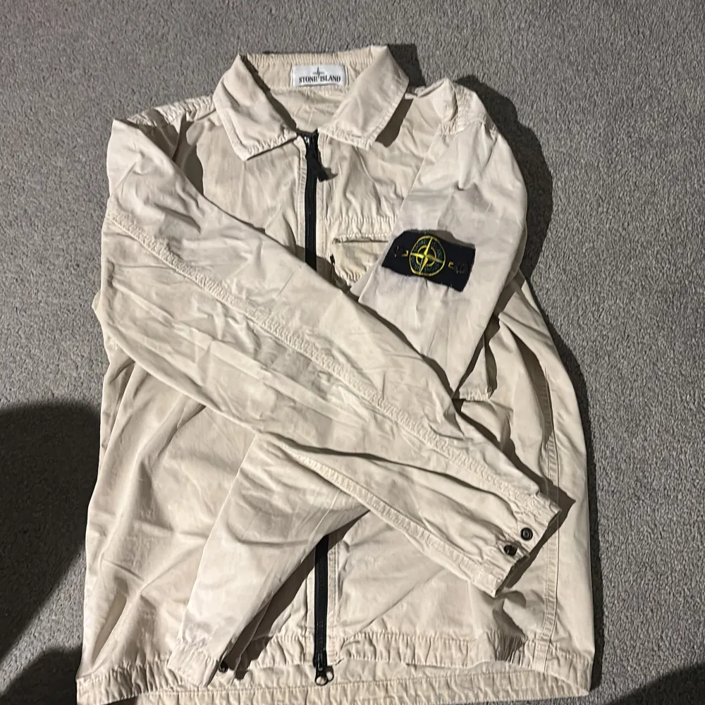 Säljer en snygg beige jacka från Stone Island. Den har en dragkedja framtill och det ikoniska Stone Island-märket på ärmen. Perfekt för vår och höst med sin stilrena design. Jackan är i bra skick och passar till många olika outfits. Självklart äkta. Nypris 4000. Jackor.