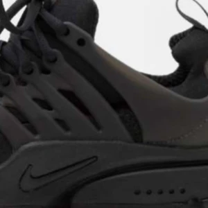 Svarta Nike Presto sneakers - Snygga svarta Nike Presto sneakers med en stilren design. Skorna har en flexibel och bekväm passform med snörning och en diskret Nike-logga på sidan. Perfekta för både vardag och träning.