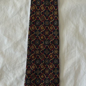 Vintage Salvatore Ferragamo Silkeslips - Salvatore Ferragamo silkeslips – sällsynt och ikonisk  Säljer denna exklusiva bruna Salvatore Ferragamo-slips i 100% silke, med ett unikt mönster. En klassisk lyxdesign som ger en elegant touch till varje outfit.  🔹 Märke: Salvatore Ferragamo 🔹 Material: 100% silke 🔹 Färg: Brun 🔹 Skick: Utmärkt – slipsen är något smutsig men behöver bara en enkel rengöring 🔹 Sällsynt modell – går inte att hitta någon annanstans online!  Perfekt för både formella tillfällen och som ett statement-piece. Tveka inte