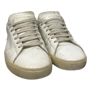 Vita sneakers från Saint Laurent - Snygga vita sneakers från Saint Laurent med röd detalj på hälen. Skorna har snörning och en klassisk design med en robust sula. Perfekta för en stilren look.