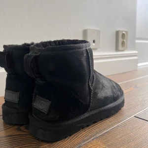 Svarta boots från UGG - Säljer ett par svarta boots från UGG i mocka. De har en klassisk design med rund tå och en bekväm sula. Perfekta för kyligare dagar. Lite slitna men inga hål eller skador.