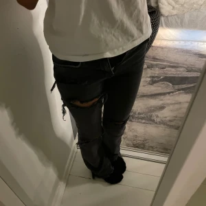 Svarta slitna jeans - Snygga svarta jeans med slitningar på låren och knäna. De har en klassisk femficksdesign och en rak passform. Perfekta för en avslappnad look med en t-shirt eller hoodie.