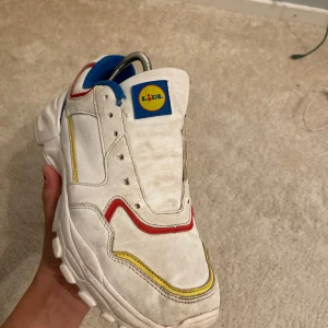  Lidl skor - Unika vita sneakers från Lidl med färgglada detaljer i rött, gult och blått. Skorna har en robust sula och en bekväm passform. Perfekta för den som vill sticka ut med en annorlunda stil.