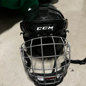 Svart hockeyhjälm CCM - Säljer en svart hockeyhjälm från CCM med galler. Hjälmen har justerbar passform och är perfekt för ishockey. Den har ventilationshål för bättre luftflöde och en robust konstruktion för extra skydd.