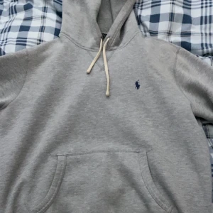 Grå hoodie från Polo Ralph Lauren - Säljer en stilren grå hoodie från Polo Ralph Lauren med den klassiska loggan broderad på bröstet. Tröjan har en bekväm passform med långa ärmar och en praktisk magficka. Perfekt för en avslappnad look. Skick 9/10. Pris kan diskuteras.