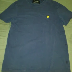 Blå t-shirt från Lyle & Scott - Säljer en blå t-shirt från Lyle & Scott med ett broderat logga på bröstet. Tillverkad i 100% bomull. Perfekt för en avslappnad stil.