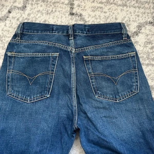 Blå jeans från Diesel - Snygga blå jeans från Diesel med klassisk femficksdesign och knappgylf. Jeansen har en rak passform och är perfekta för en avslappnad stil. Märkesdetaljer syns på fickan och insidan av linningen.