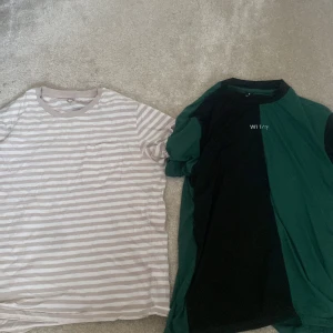 Två t-shirts i randigt och grönt/svart - Säljer två t-shirts. Den ena är randig i beige och vit med korta ärmar och rund hals. Den andra är i grönt och svart med texten 'WHAT' på bröstet, också med korta ärmar och rund hals. Perfekta för en avslappnad stil.
