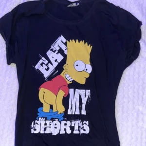 Svart t-shirt med Bart Simpson-tryck - Cool svart t-shirt med ett stort tryck av Bart Simpson och texten 'Eat My Shorts'. Perfekt för fans av The Simpsons. 