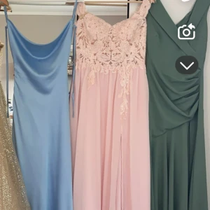 Rosa långklänning med spetsdetaljer - Elegant rosa långklänning med spetsdetaljer på överdelen och axelbandslös design. Perfekt för bal eller festliga tillfällen. Klänningen har en flytande kjol som ger en romantisk känsla. Även en slits som går upp gentemot benet.