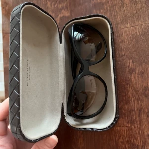 Svarta solglasögon från Bottega Veneta - Snygga svarta solglasögon från Bottega Veneta med en elegant flätad detalj på skalmarna. De har en klassisk och tidlös design som passar perfekt för alla tillfällen. Kommer med ett stilrent fodral.jag köpte den på ett aktion i Frankrike. 