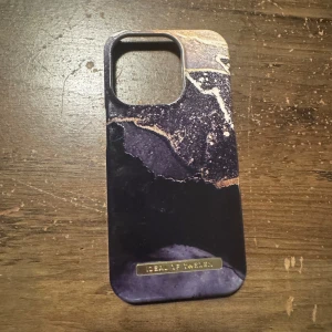 Marmormönstrat mobilskal från Ideal of Sweden - Snyggt mobilskal med marmormönster i svart, lila och guld från Ideal of Sweden. Skalet har en elegant design med en metallisk detalj längst ner. Perfekt för att ge din mobil en stilfull look.