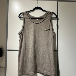 Grå linnetopp från Adidas - Säljer en grå linnetopp från Adidas med svart kant runt ärmhål och hals. Adidas-loggan är broderad på bröstet. Skön och luftig passform.