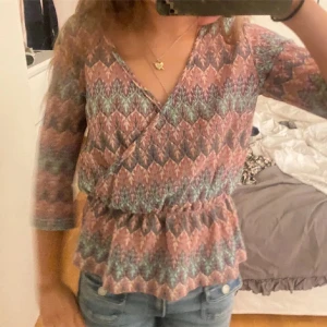 Mönstrad omlottopp - Säljer en färgglad omlottopp med ett unikt mönster i rosa, blått och grönt. Toppen har trekvartsärmar och passar jätte funt till våren