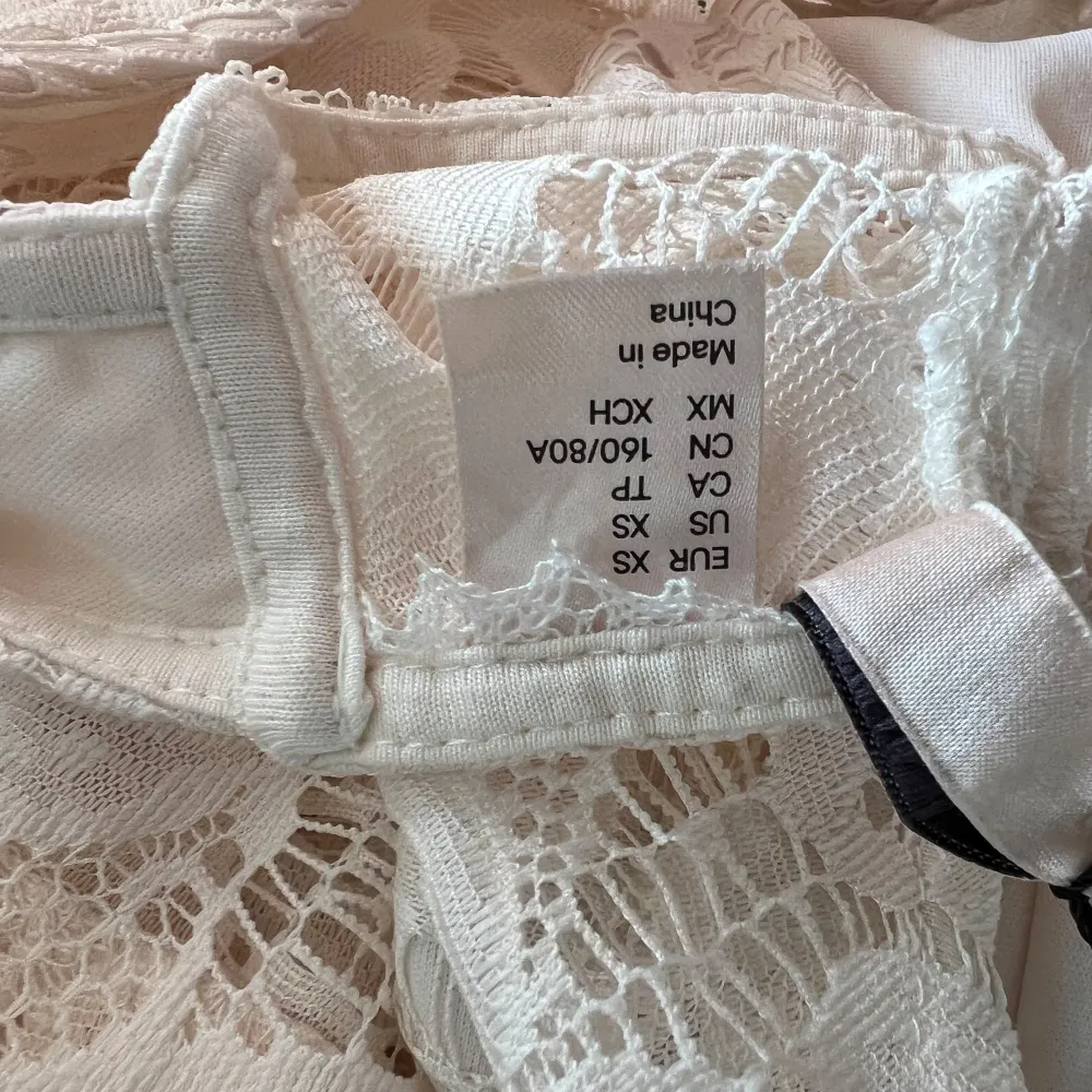 Säljer en elegant vit spetsklänning med vackra detaljer. Klänningen är ärmlös och har en öppen rygg med knytning. Perfekt för sommarens festligheter. Den har en lång längd och ett fint mönster i spets.. Mekot.