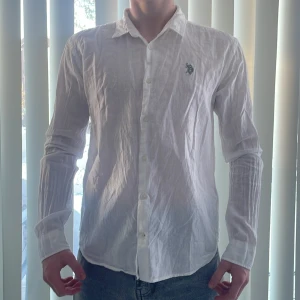 Vit linneskjorta från U.S. Polo Assn. - Säljer en stilren vit linneskjorta från U.S. Polo Assn. med broderad logga på bröstet. Skjortan har långa ärmar och knappar framtill. Perfekt för en avslappnad men ändå elegant look  👀 