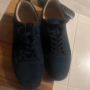 Marinblåa sneakers från Christian Louboutin - Snygg marinblå sneakers från Christian Louboutin med klassisk design och snörning. Skorna har en vit sula med märkets logotyp ingraverad. Perfekta för en stilren look.