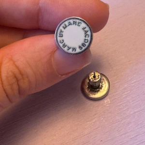 Vita örhängen från Marc Jacobs - Snygga vita örhängen från Marc Jacobs med klassiska runda designen och märkets namn ingraverat runt kanten. Använda men i bra skick. 