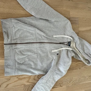 Grå huvtröja från Polo Ralph Lauren - Säljer en stilren grå huvtröja från Polo Ralph Lauren. Tröjan har vita snören och svart polo märke.