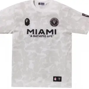 Säljer en supercool vit fotbollströja från samarbetet mellan A Bathing Ape och Miami. Tröjan har ett unikt och korta ärmar. Den har tryck med 'MIAMI' och 'A BATHING APE' på framsidan, samt loggor på bröstet och ärmen. Perfekt för dig