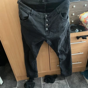 Jeans från Ellos  - Ett par svarta ”tvättade” jeans från Ellos i storlek 44, ganska korta i benen. Knappar hela vägen upp istället för dragkedja 
