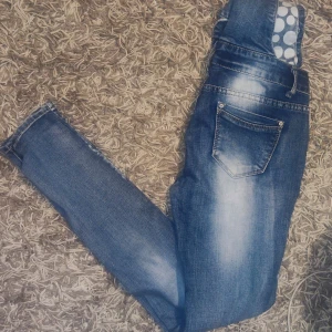 Jeansbyxdress med prickiga detaljer - Säljer en snygg jeansbyxdress med coola prickiga detaljer på hängslena. Byxdressen har en klassisk blå jeansfärg med snygga slitningar och knappar framtill. Perfekt för en avslappnad och trendig look!