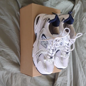 Vita och marinblå sneakers från New Balance - Säljer ett par snygga New Balance 530 sneakers i vitt och marinblått i fint använt skick! De har en sportig design med meshmaterial för bra andningsförmåga och en stabil sula för komfort. Perfekta för både vardag och träning!