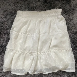 Vit prickig kjol med volang - Säljer en superfin vit kjol från FB Sister. Den har ett sött prickigt mönster och volanger som ger en romantisk känsla. Perfekt för sommardagar eller en festlig kväll! Kjolen är i storlek L och har en elastisk midja för extra komfort.