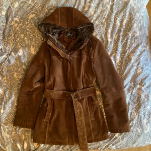 Brun mockajacka med pälsfoder från Petroff - Säljer en snygg brun mockajacka från Petroff i storlek 38. Jackan har ett mjukt pälsfoder i huvan och ett bälte i midjan för en perfekt passform. Den är långärmad och perfekt för höst och vinter. Jackan är i bra skick och redo för nya äventyr!