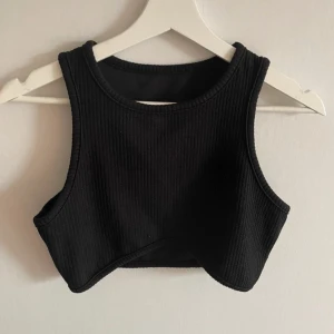 Svart ribbad croppad topp från Shein - Säljer en snygg svart ribbad croppad topp från Shein. Perfekt för sommardagar eller att ha under en kavaj för en cool look. Toppen är ärmlös och har en tight passform som framhäver figuren. Superbekväm och lätt att matcha med olika outfits!