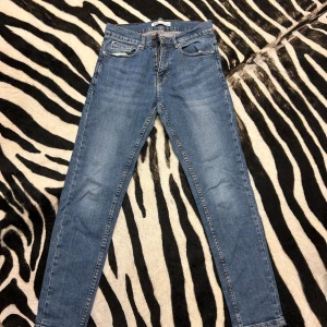 Blå jeans från Zapa - Säljer ett par snygga blå jeans från Zara. De har en klassisk design och en dragkedja med knapp framtill. Jeansen är i en slim passform och har en skön midwaist. Perfekta för vardag!