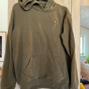 Olivgrön hoodie från Lyle & Scott - Säljer en olivgrön hoodie från Lyle & Scott i storlek 14/15 år. Den har en stor ficka framtill. Perfekt för höst och vår, och den är superbekväm att ha på sig. Färgen är aningen mörkare än den ser ut på bilderna. Begagnat skick.