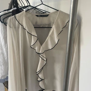 Blus från Zara - Volangblus från Zara i vit med svarta detaljer. Så fin och smickrande! Möts upp i Sthlm, annars står köparen för frakten 🩷