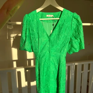 Grön klänning DryLake - En oanvänd cocktailklänning från DryLake i storlek M, prislapp sitter kvar. Puffärmar som går till halva överarmen, längd på klänningen är till halva låret (jag är 170cm) och den knäpps framtill med tryckknappar. 