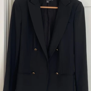 DKNY kavaj - DKNY kavaj i ull. Storlek 4 US. Normal passform. Stängs med knappar. Fyra guldfärgade knappar fram och fyra vid ärmsluten. Två fickor fram. Det finns matchande byxor till. Se separat annons. I mycket fint skick. 