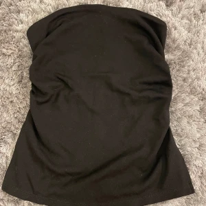 Svart tubtopp från Bershka - Säljer en stilren svart tubtopp från Bershka. Den är perfekt för sommardagar eller en utekväll. Toppen är i ett mjukt och stretchigt material som sitter bekvämt på kroppen. Den har en enkel design utan axelband och en liten slits på sidan för extra stil. Passar perfekt till både jeans och kjol!