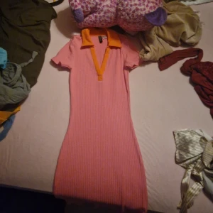 Rosa ribbad klänning med orange detaljer - Säljer en superfin rosa ribbad klänning med en cool orange krage och v-ringning. Den är kortärmad och har en tight passform som verkligen framhäver figuren. Perfekt för sommardagar eller en utekväll med vänner!