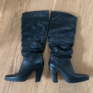Svarta skinnstövlar med klack - Säljer ett par svarta stövlar i skinn med hög klack. Perfekta för både höst och vinter. Stövlarna har en bekväm passform och är i okej skick, även om det finns lite slitage på klacken. Lätt att lämna in och klacka om. Stora i stl, mer 37 än 36