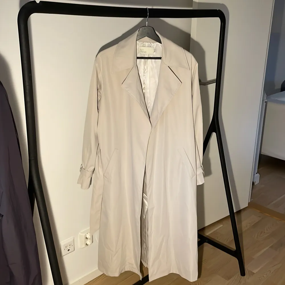 Säljer en snygg beige oversize trenchcoat från NLY Trend i storlek 34. Den har en klassisk design med långa ärmar och ett bälte i midjan för en stilren look. Perfekt för vår och höst! Nypris: 1200kr. Jackor.